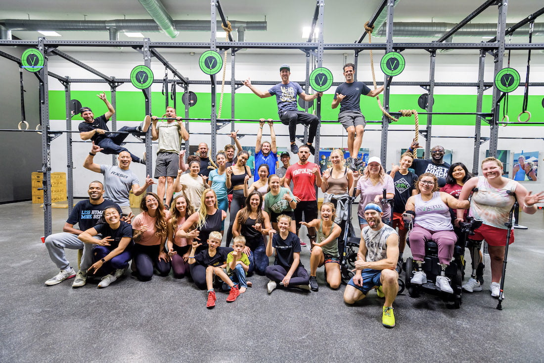 Group picture of the 2021 Beautifully Flawed and Forge retreat attendees smiling big in the crossfit gym after completing workouts adaptively.