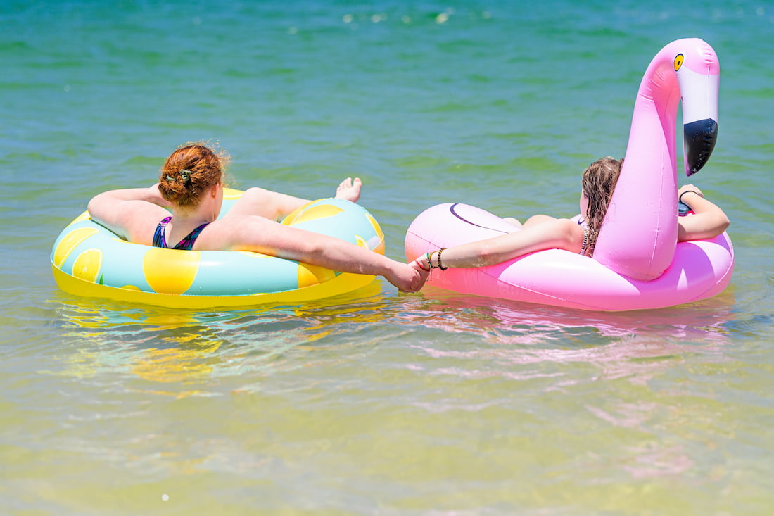 Two Beautifully Flawed attendees relax in their inflatable floats and stay close together by holding hands, enjoying the warm ocean waters of Kauai.