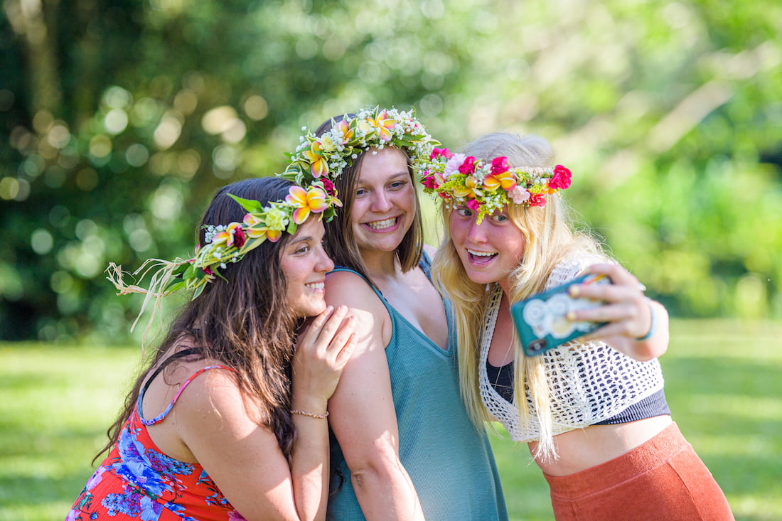 Three young women wearing their colorful, flower haku leis gather together to take a selfie to remember the special moment.