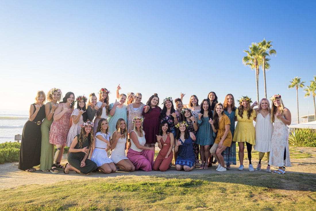 Group photo of all the Beautifully Flawed retreat attendees with Bethany Hamilton smiling and laughing after making their haku leis with the ocean in the background.