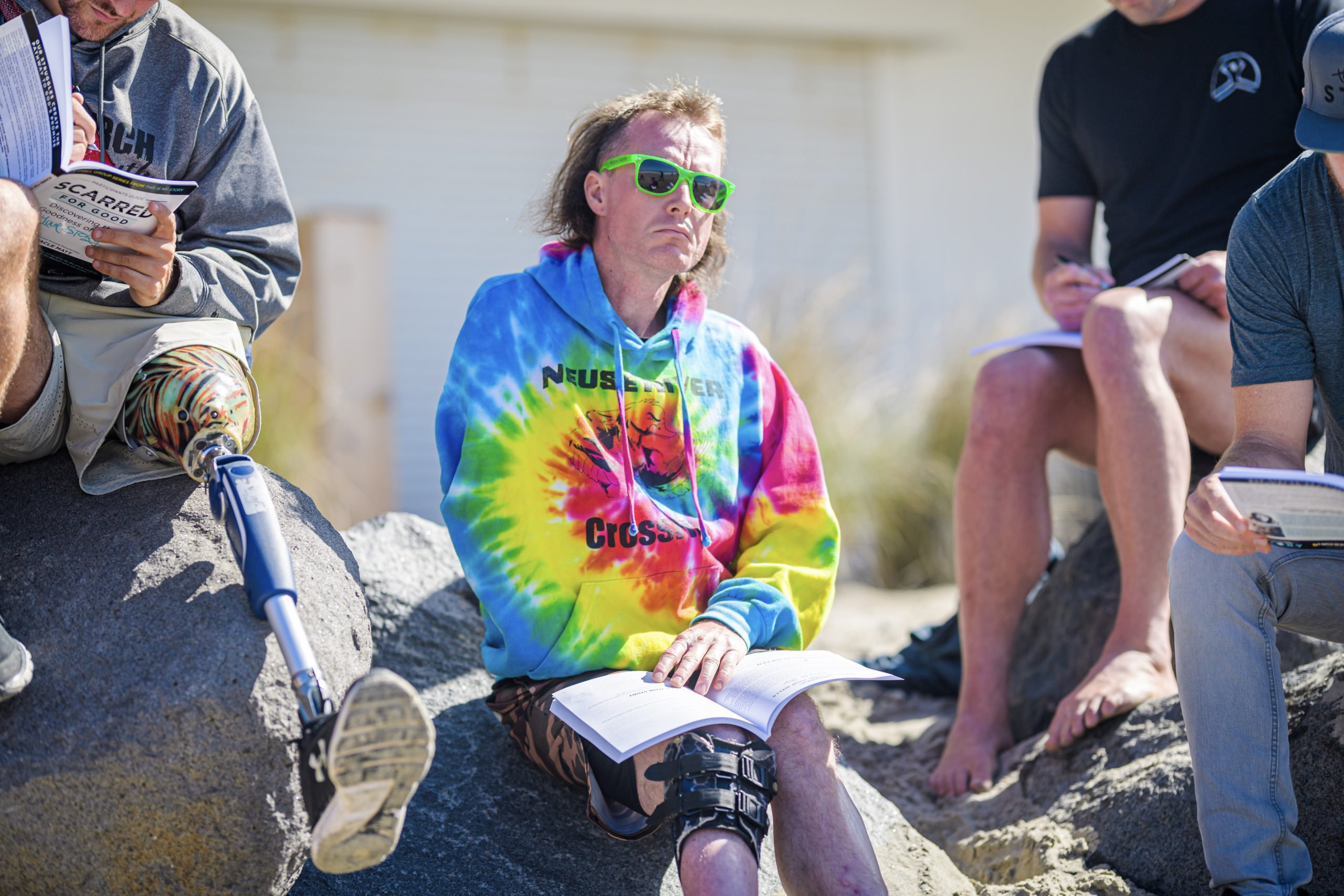 Shane pensively thinking while sitting on a rock at the beach with the other Forge men holding the devotional books they're working through during the group sessions.