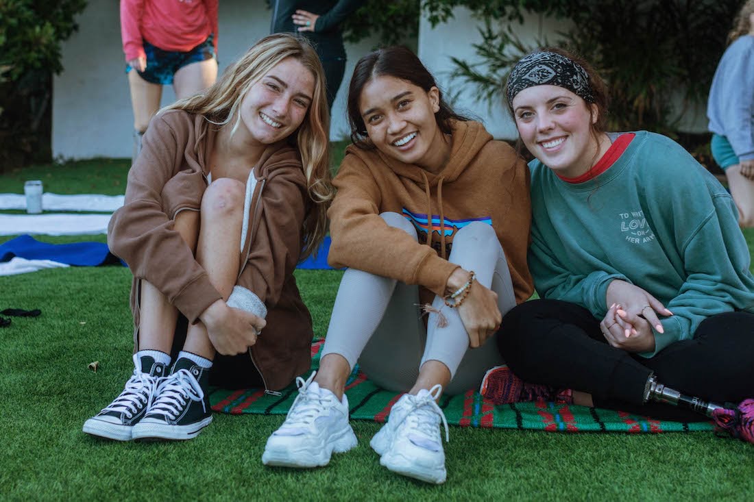 Ellice and two other young women amputees smile and lean close together for a group photo during a morning workout in the backyard.