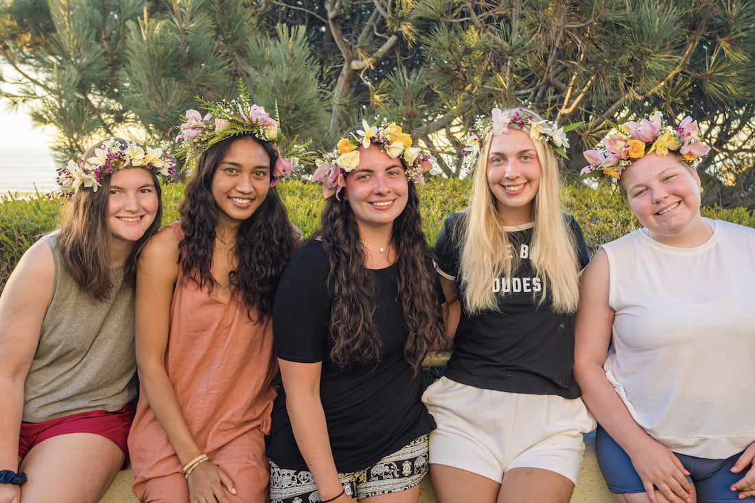A group photo with Ellice and four other young women at the retreat smiling and showing off their haku leis they just made.