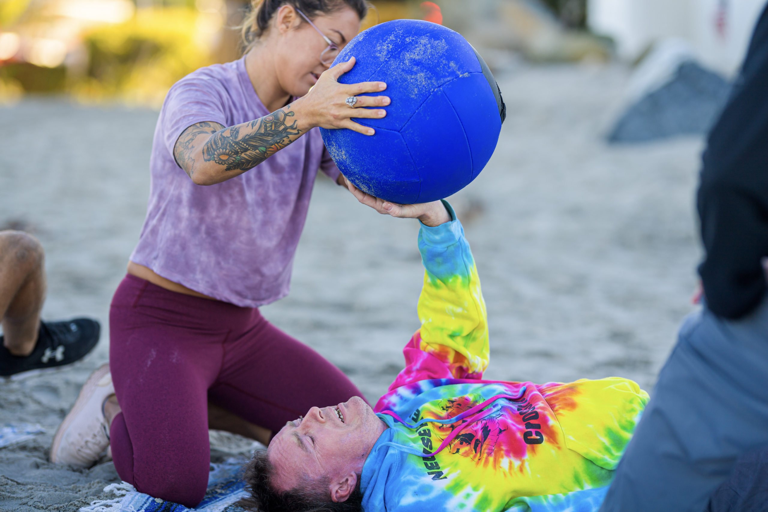 During a morning workout on the beach, Shane attempts the challenge of lifting a medicine ball with his one arm while laying on a beach towel.