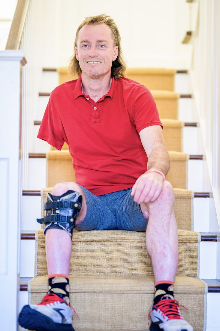 A smiling portrait of Forge attendee Shane sitting on a flight of stairs in a house.