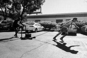 Black and white, side-angle photo of Shane completing a workout pulling a weighted sled through the parking lot.