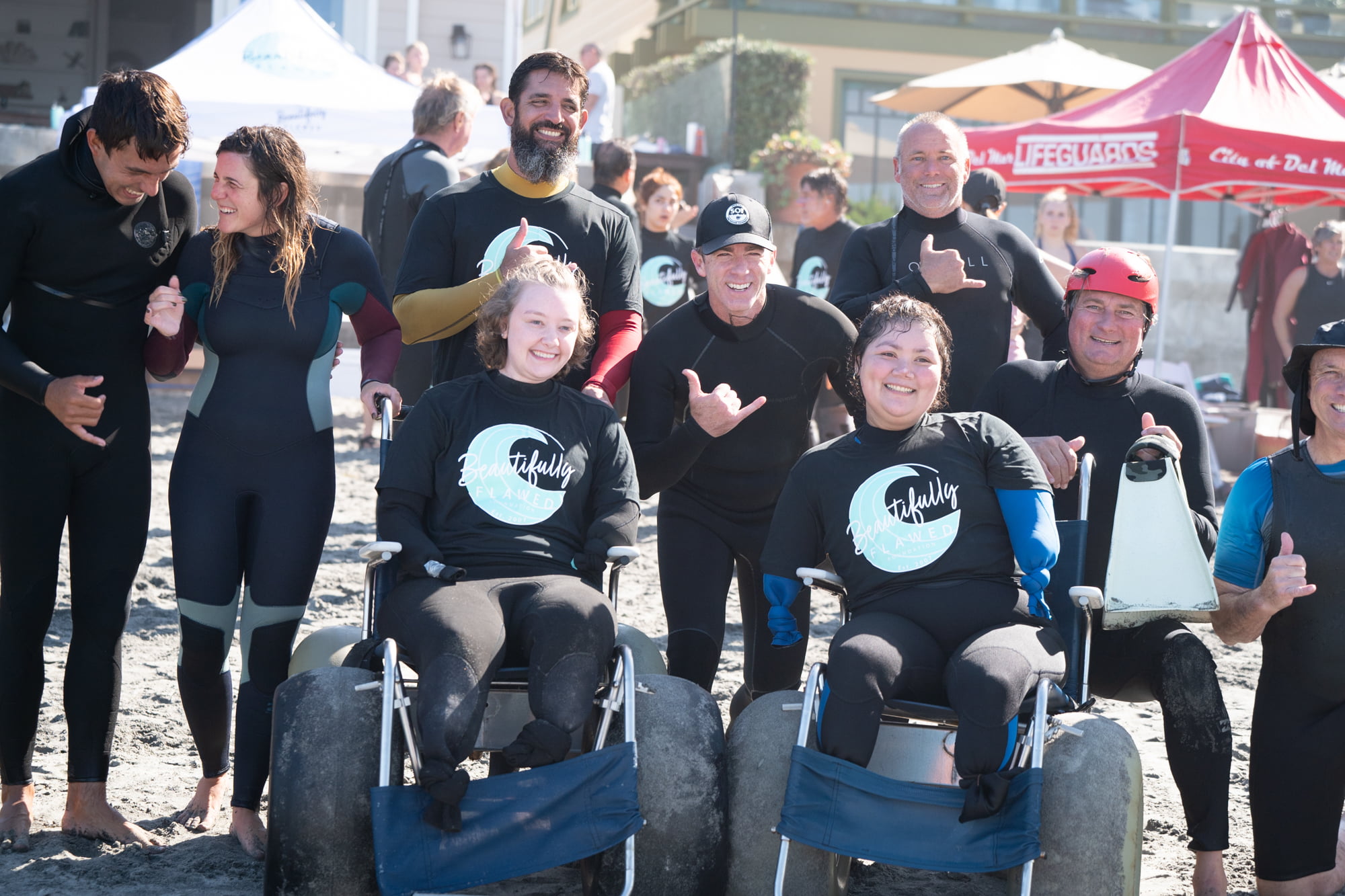 Two young women quad amputees smile and give shakas with their instructors before they get into the ocean to learn how to surf.