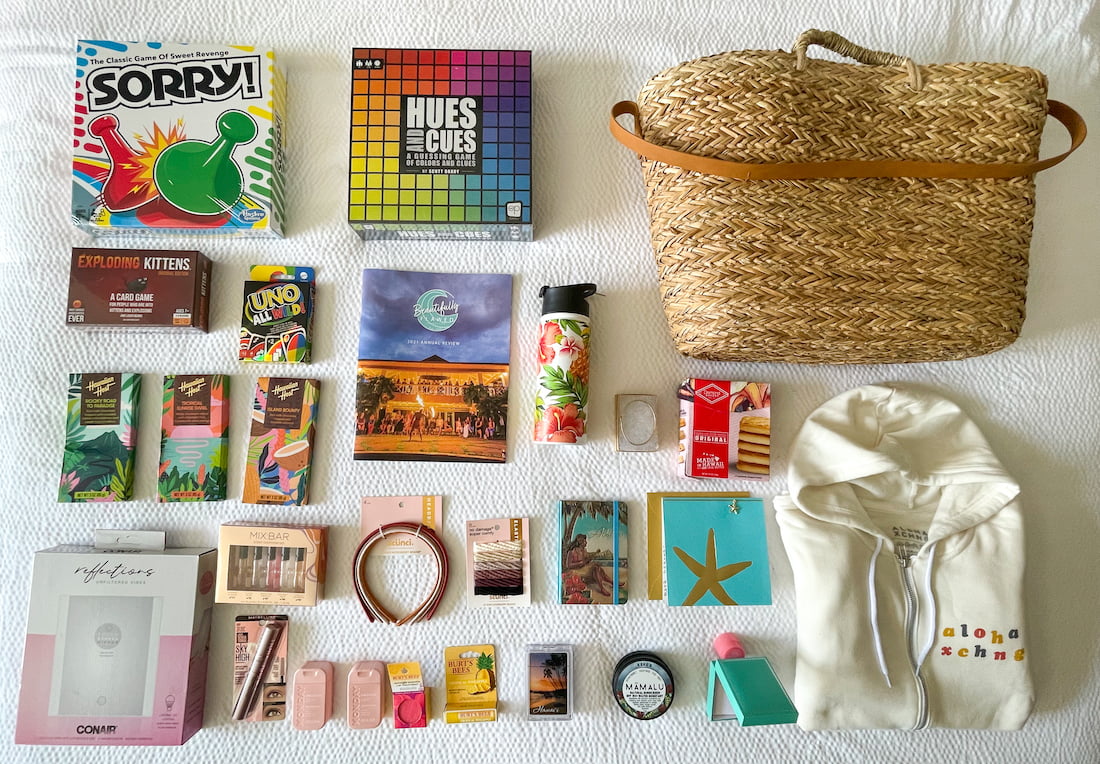An assortment of gifts including board games, a rattan beach tote, sunscreen and zip up hoodie from Kauai, hair and makeup accessories, chocolate, and Beautifully Flawed swag for Ainsley.